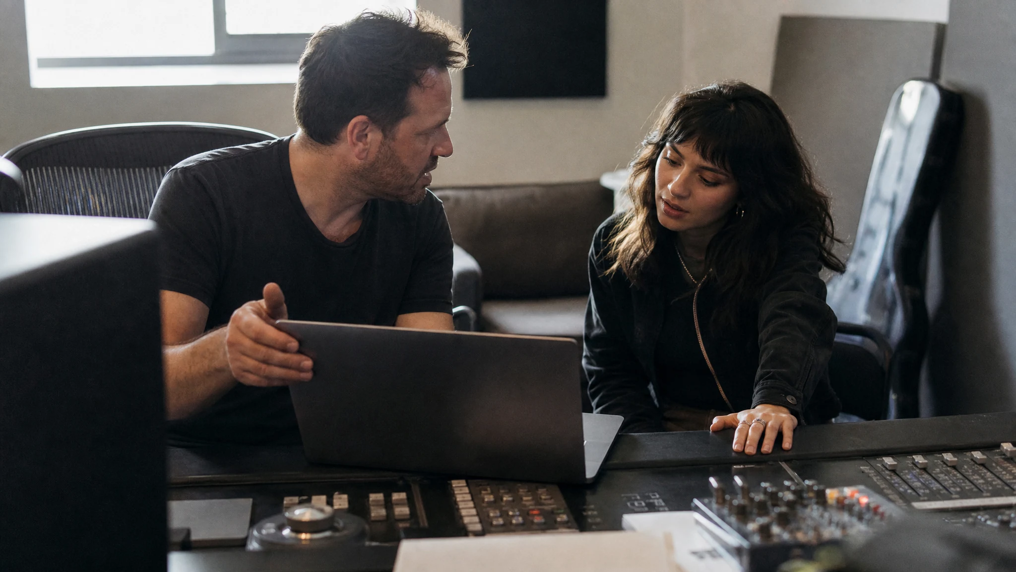 A mixing engineer and a client talking across a studio desk in a small mixing room